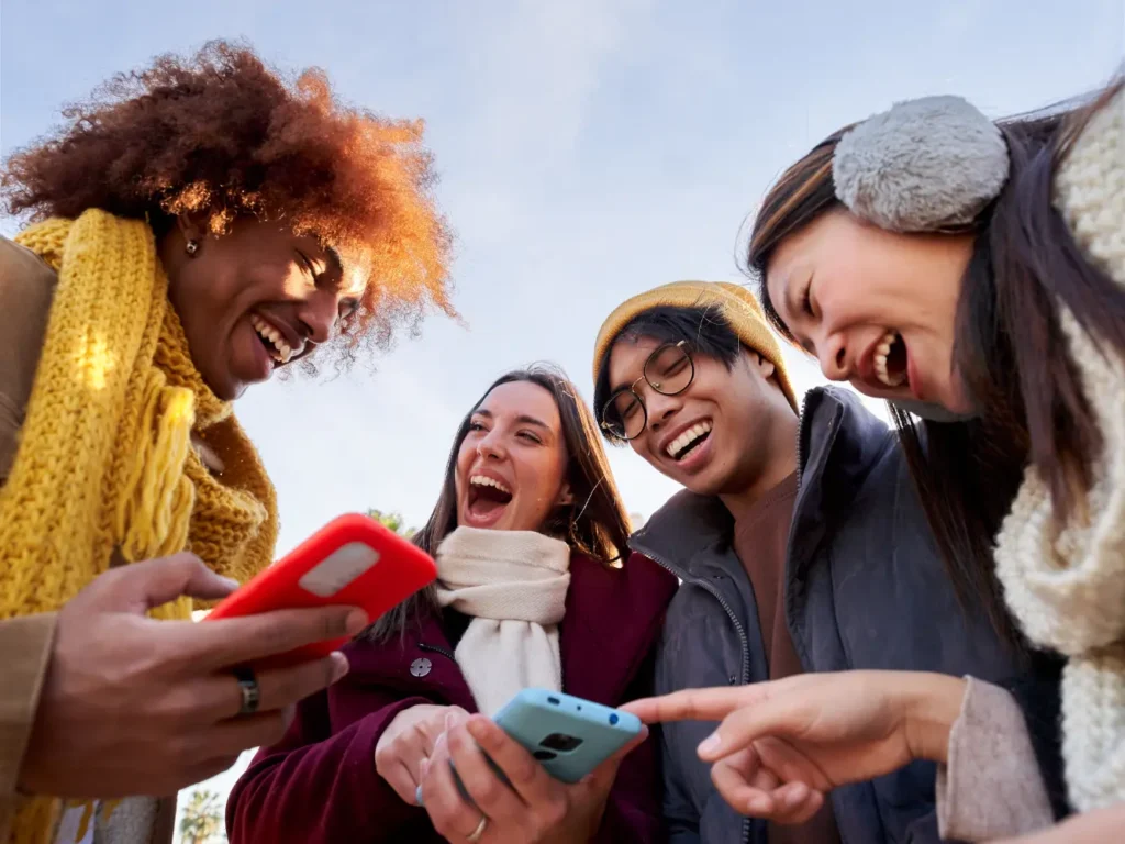 OnlyFans Management Services: Group of four young friends laughing while looking at content on their mobile phones outdoors