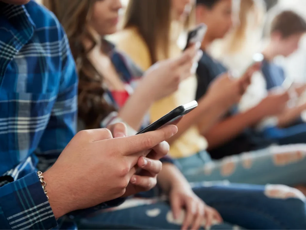 OnlyFans Management Services: Group of teenagers sitting in a row simultaneously using their mobile phones